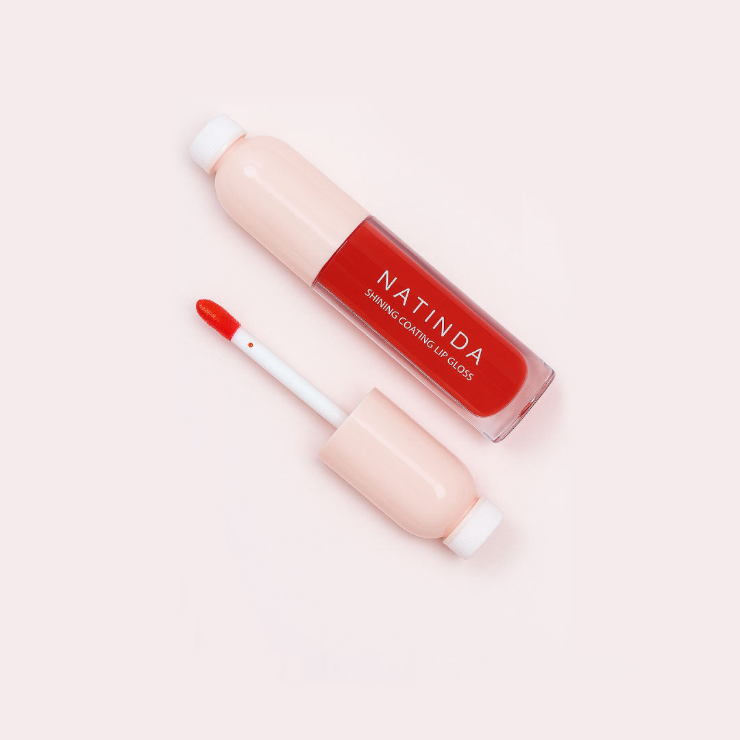 Lip gloss with red liquid and beige applicator on a light pink background