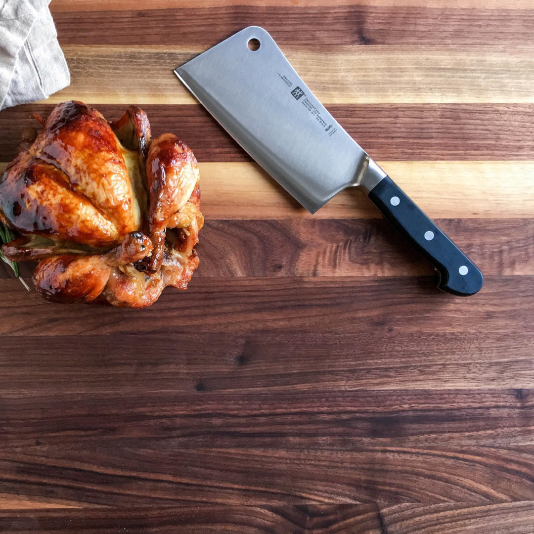 Zwilling stainless steel meat cleaver placed on wooden cutting board beside roasted chicken